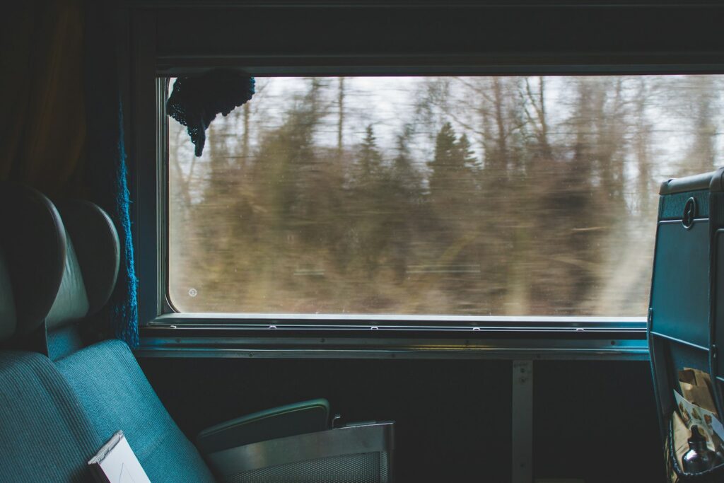 Reiziger met koptelefoon kijkt uit het raam van een trein
