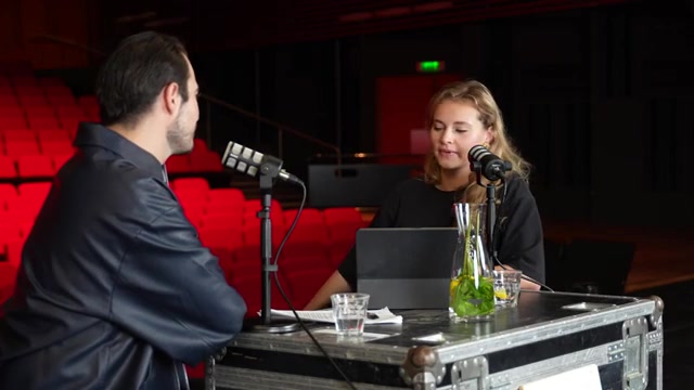 Vajèn van den Bosch en Milan van Waardenburg aan tafel met microfoons in een theaterzaal