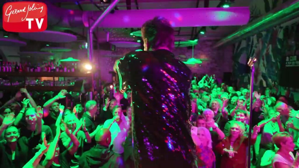 Gerard Joling in een glitterjasje op het podium voor een uitzinnig publiek
