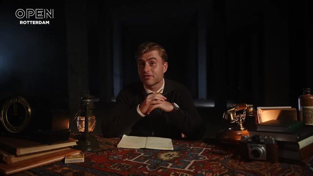 Presentator Jeroen Heidenreich aan een bureau met oude boeken en een lantaarn in een donkere kamer